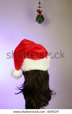 waiting under mistletoe for a Christmas kiss is a brunette in a santa hat