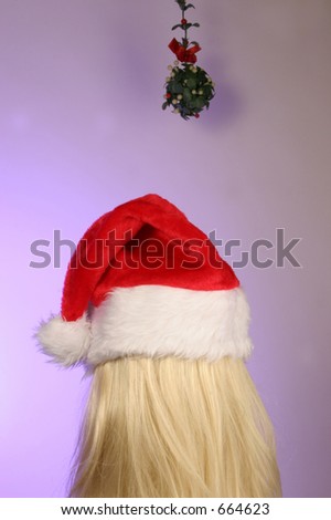 blonde in a santa hat waiting under mistletoe for a Christmas kiss