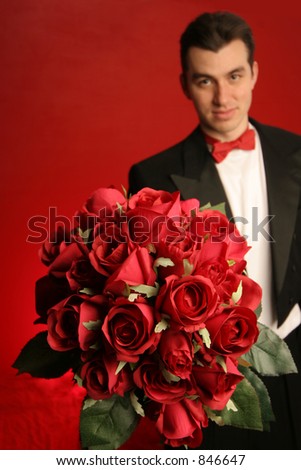 man holding out large bouquet of red roses in formal black tux with red bow tie