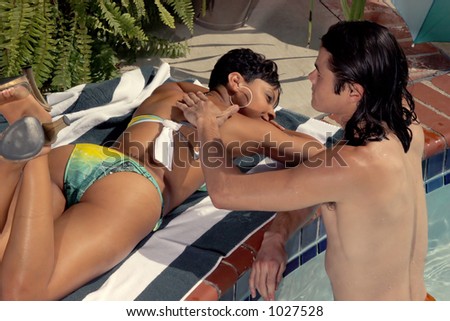he is putting on her suntan lotion at the pool