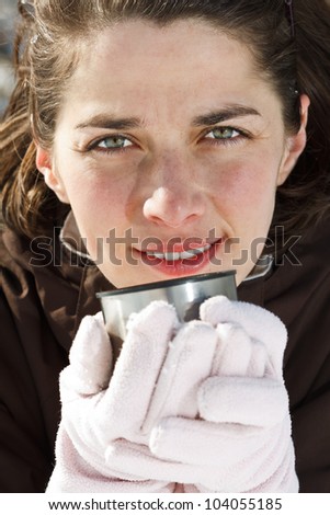 Close-up of a beautiful young woman wearing gloves, holding a cup of hot drink, smiling into camera - outdoors