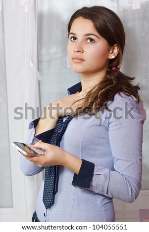 Portrait of a beautiful teenage girl with long brown hair in pony tail, looking up daydreaming, holding her mobile phone, indoors