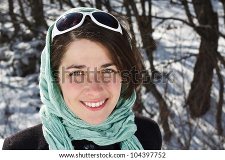 Portrait of a beautiful young woman wearing scarf and sunglasses, smiling into camera - winter forest in background