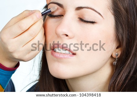 Portrait of a beautiful young woman with brown hair, somebody else is doing her make-up, painting eyelids, eyes closed - isolated on white