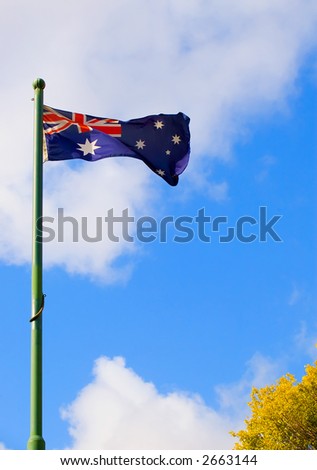 An Australian flag flying on a flag pole against a blue shy with some clouds