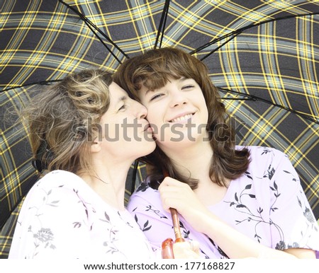 Mother kisses the daughter under a checkered umbrella