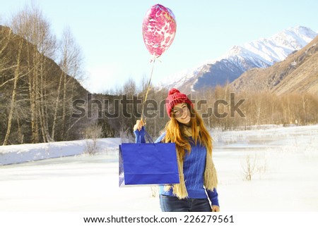 cheerful girl with a balloon and a package with a gift on the background of snowy mountains