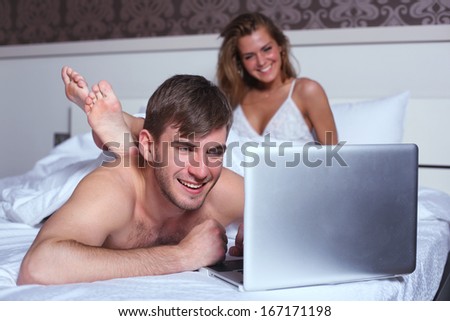 Couple with laptop in bed. Man at computer, woman  looking at man.