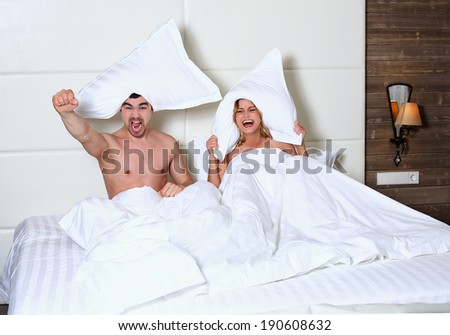 Man and woman sitting in bed with a pillow over his head