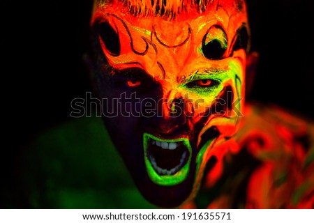 Man\'s face with fluorescent body art. Black background.