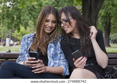 Two Beautiful Young Woman Browsing Smart phone In A Park