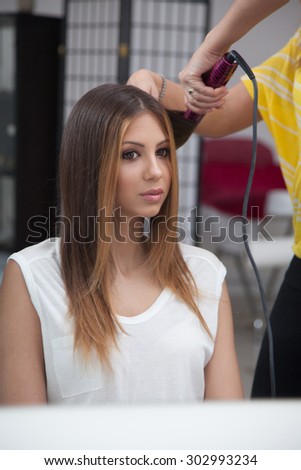 Beautiful young lady straightener her hair at the hairdresser salon.