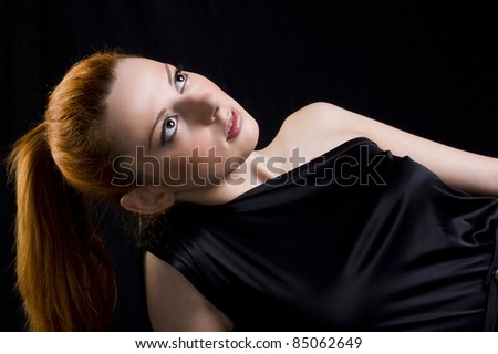 beautiful young woman in a black dress with a black background, and is looking up
