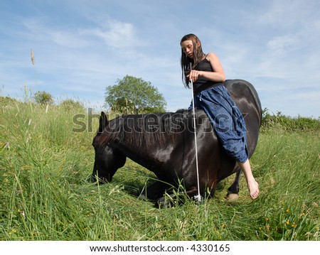 young woman and her black horse laid down in a field