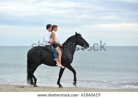 beautiful black stallion on the beach with young couple