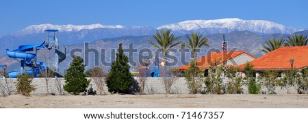 A playground slide is shown at a city park in Hemet, California with snow covered Mount San Gorgonio in the background.