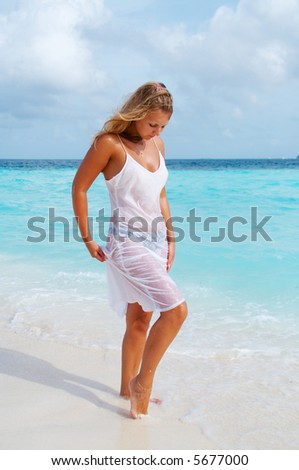 Woman in wet gauzy dress on white sand beach. Maldives.