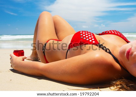 Young girl in red bikini is lying on white sand beach and drinking soda