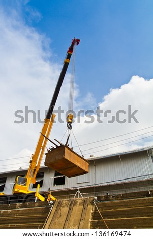 Yellow mobile crane hydraulic boom raises tray over dry dock