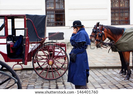 VIENNA, AUSTRIA - JUNE 4: Female coachman in a vintage dress talk on a mobile phone near the horse-drawn carts on June 4, 2013 in Vienna. Vienna attracts about five million tourists a year