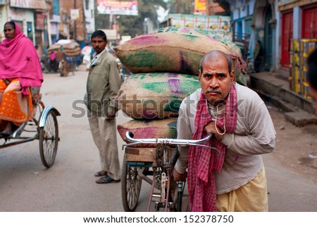 VARANASI, INDIA - JANUARY 1:Indian loader works hard and carries bags of cargo on an old bicycle in the oldest asian city on January 1, 2013. Varanasi urban agglomeration had a population of 1,435,113