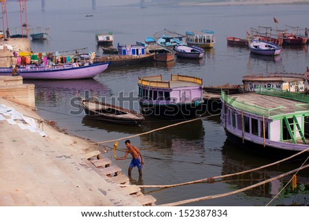 VARANASI, INDIA - JANUARY 1: Man washes clothes at morning on the banks of the river Ganges with old boats around on January 1, 2013. Varanasi urban agglomeration had a population of 1,435,113.