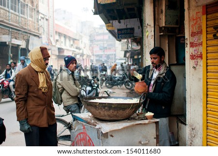 VARANASI, INDIA - JANUARY 4: People watch with attention to the seller of street food at the cold morning on January 4, 2013 in Varanasi. Varanasi urban agglomeration had a population of 1,435,113