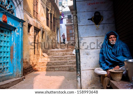 VARANASI, INDIA - JAN 4: Elderly man in a cape sitting alone on the street of the ancient indian city on January 4 2013. The 2,525 km Ganges river rises in Indian Uttarakhand & flows into Bangladesh