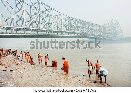 KOLKATA, INDIA - JAN 19: Many people bathing in river Hooghly under the busy Howrah bridge on January 19, 2013 in Calcutta. Howrah bridge bears 100,000 vehicles and more than 150,000 people every day