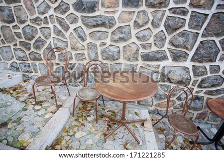 Round table and some chairs standing at stone wall of cafe