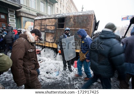KIEV, UKRAINE - JAN 21: Active protester with shield and mask stands near the burned military auto on the winter street during anti-government riot Euromaidan on January 21, 2014, in Kyiv, Ukraine.