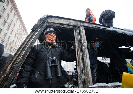 KIEV, UKRAINE - JAN 21: Young protester with binoculars in mask watch from a broken window of burned military car during anti-government protest Euromaidan on January 21, 2014, in Kyiv, Ukraine