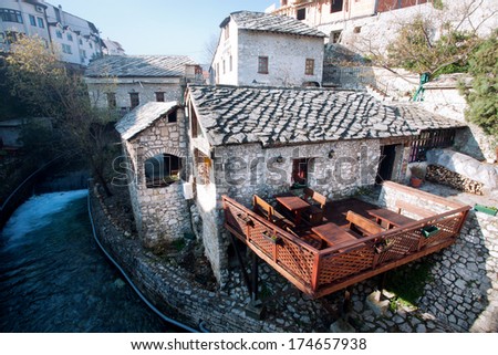 MOSTAR, BOSNIA AND HERZEGOVINA - DEC 28: Wooden terrace restaurant with white stone walls over the river in old town on December 28, 2013. 45% of the country\'s population are Muslims, 36% are Orthodox