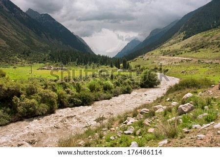 Bright sunshine before the storm illuminates powerful river in a valley between the mountains