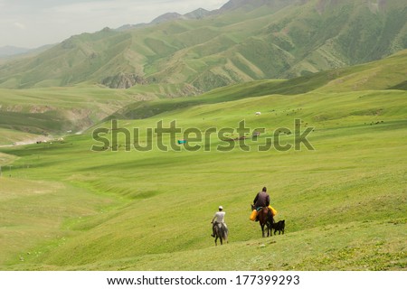 Two riders on horseback go away in the valley between the green mountains