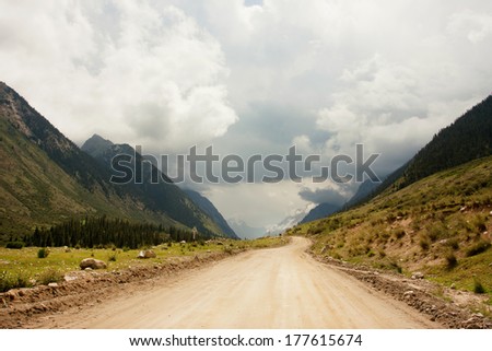 Rural road between the mountains of Central Asia with big clouds in the sky for a moment before a thunderstorm