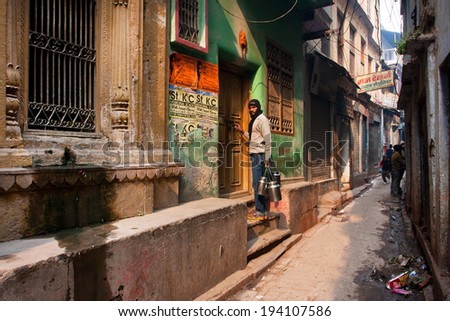 VARANASI, INDIA - JAN 6: Man with cans of water come in home in the narrow street with historical buildings on January 6, 2013. Varanasi urban agglomeration has a population of 1,435,113