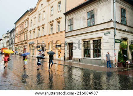 KRAKOW, POLAND - AUG 5: People with umbrellas walk through the wet street under the rain on August 5, 2014. Krakow with population of 800,000 people has 2.35 million foreign tourists annually