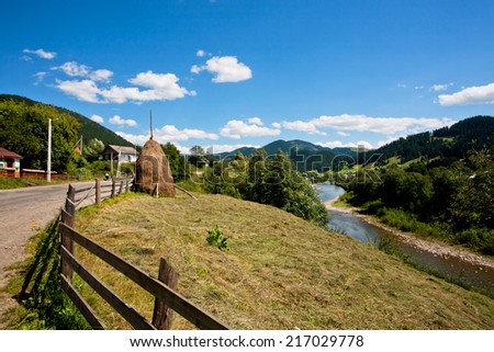 Land of a farmer near the mountain river with a shock of hay on a background of forest