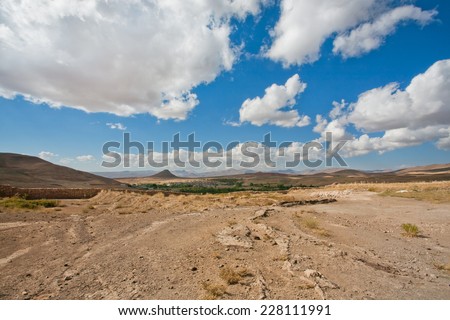 Beautiful valley in the Middle East with low mountains and small town in the distance under the white clouds on a sunny day