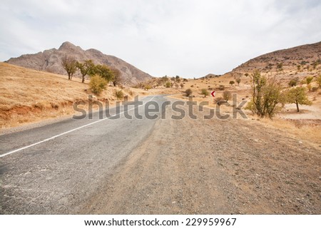 Asphalt road in a sandy valley among the mountains under gray clouds