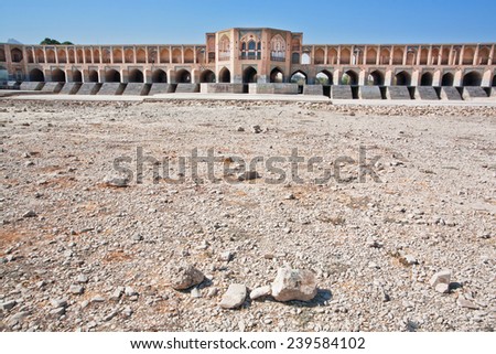 Dry soil in the bed of a dried river with the old bridge on the background in Isfahan, Iran, Middle East