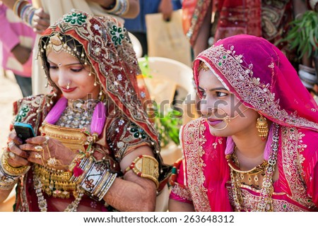 JAISALMER, INDIA - MAR 1: Women in beautiful indian dresses and gold jewelry sitting in shadow on the Desert Festival on March 1, 2015 in Rajasthan. Every winter Jaisalmer takes the Desert Festival