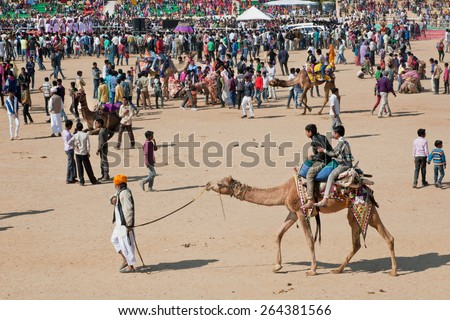 JAISALMER, INDIA - MAR 1: Crowd of people and the cameleer entertain children with camels during the rural Desert Festival on March 1, 2015. Every winter Jaisalmer takes the famous Desert Festival