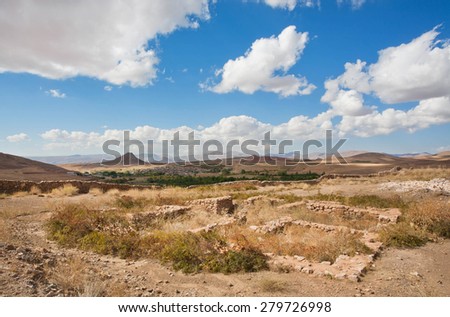 Ruined city in beautiful valley in the Middle East with low mountains in the distance under the white clouds on a sunny day