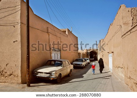 YAZD, IRAN - OCT 20: Iranian family walking past the clay houses and retro cars in deserted city on October 20, 2014. With population of 270.600 families, Yazd is the centre of Persian architecture