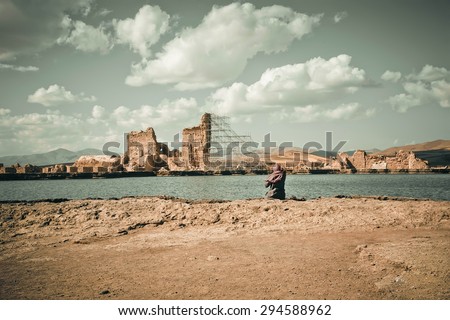 Landscape with river, ruins of historical persian city and muslim woman in hijab sitting on the river\'s bank