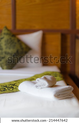 Towel on bed in hotel room to welcome guests in soft warm natural lighting