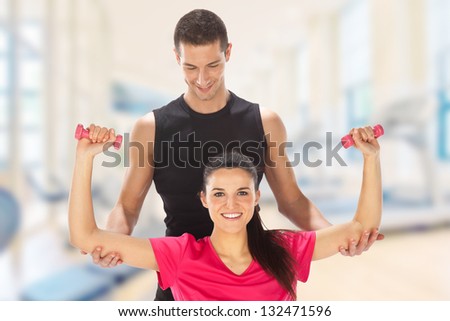 Young man and woman lifting weights./ Woman with her personal fitness trainer exercising with weights in the gym