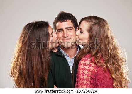 two young women kissing handsome man standing between them / Portrait of three young friends over grey background